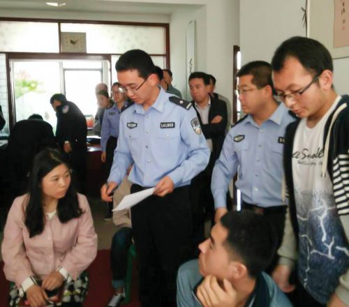 Kiinalaisia poliiseja puhumassa istuvalle naiselle ja miehelle.